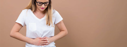 Woman in a white shirt holding her stomach, looking concerned.