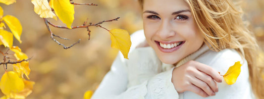 Smiling woman in a cozy sweater surrounded by autumn leaves.