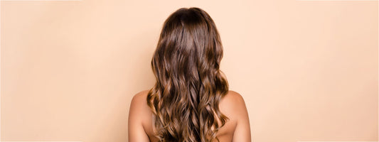 A woman with long wavy hair seen from behind against a beige background.