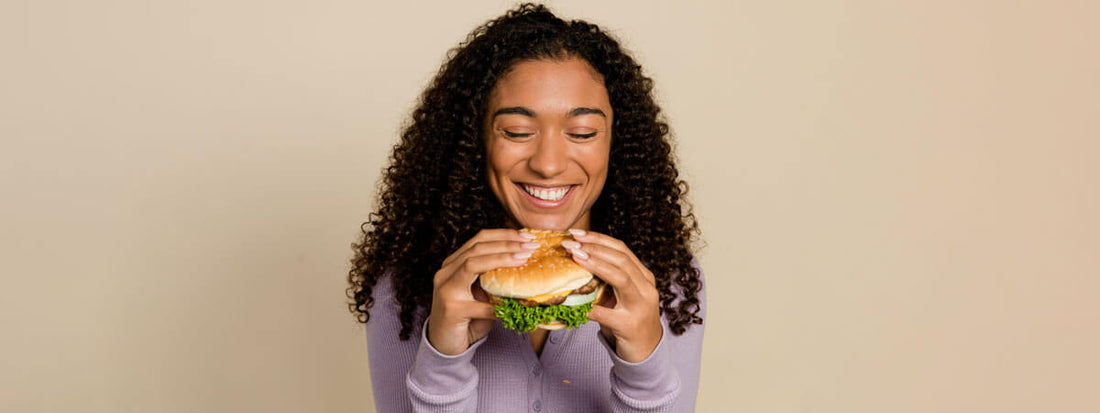 Smiling woman holding a burger against a neutral background.