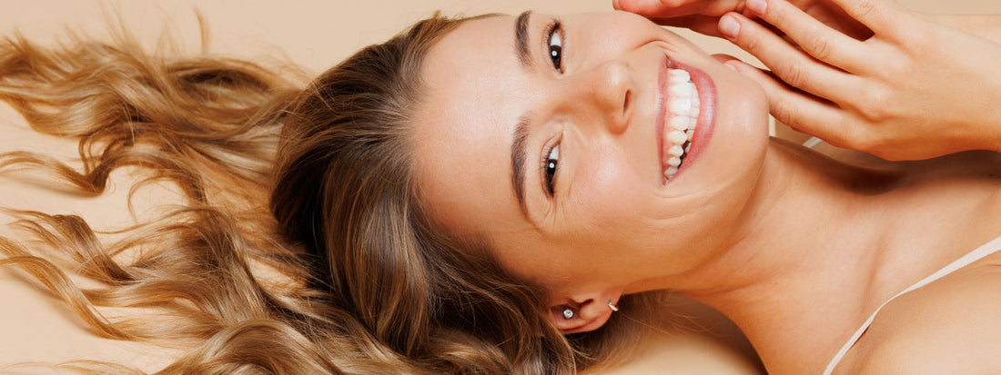 Smiling woman with long hair, lying down and touching her face.