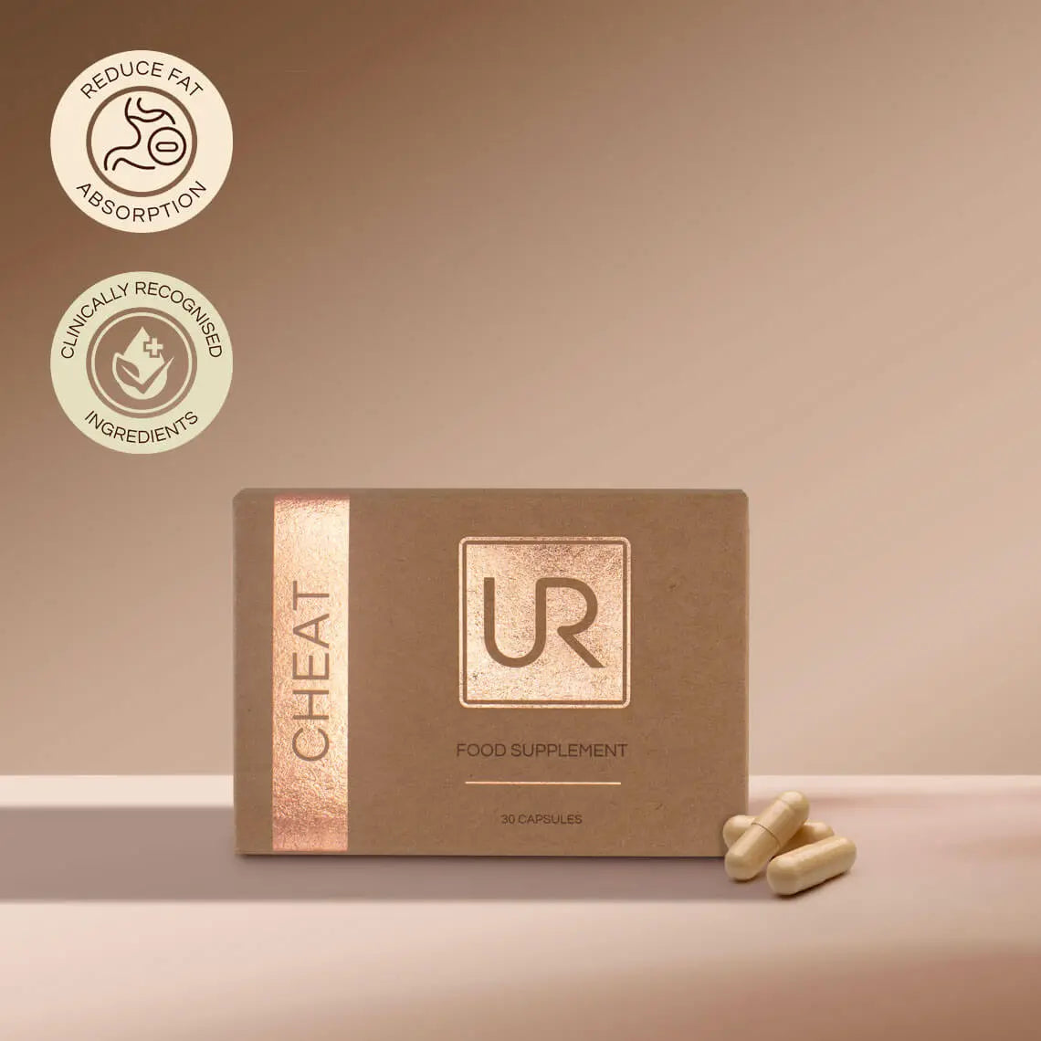 A box of UR Cheat Food Supplement capsules on a beige surface with a matching beige background. The box is brown with a metallic rose gold vertical stripe on the left and a metallic square logo on the front.