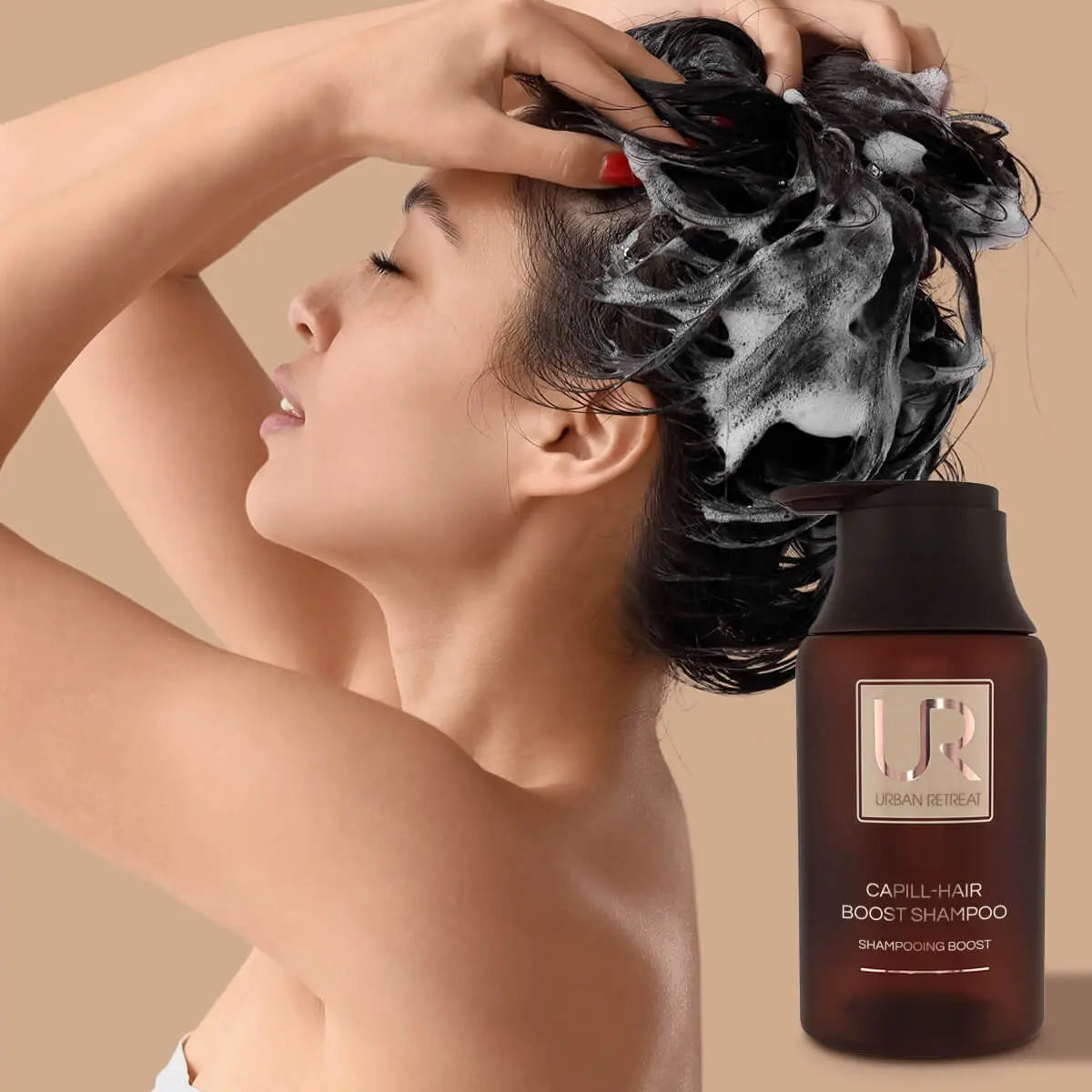A woman with dark hair covered in white shampoo lather is shown from the side, with a brown bottle labeled UR CAPILL-HAIR BOOST ENHANCING SHAMPOO placed beside her on a warm beige background.