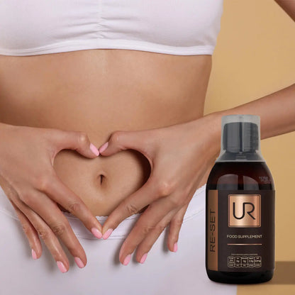 A close-up of a woman's midsection with her hands forming a heart shape around her stomach, alongside a bottle of UR Re-Set food supplement on a beige background.